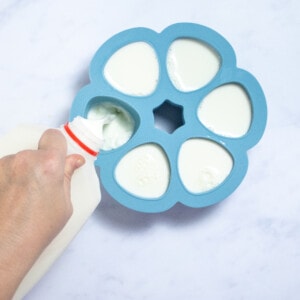 A hand holding a jug of milk poured it into a small freezer bowl tray.