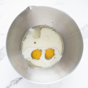 A silver mixing bowl on a marble countertop with wet ingredients for muffins.