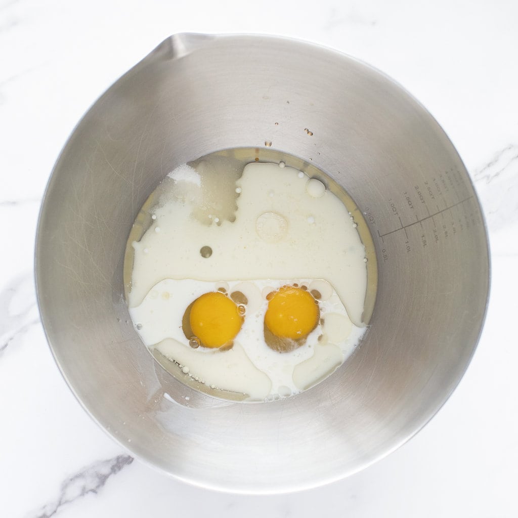 A silver mixing bowl with white ingredients for muffins on a marble countertop.