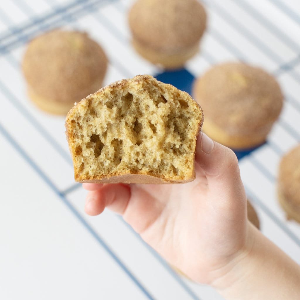 A small hand holding a cinnamon muffin against a cooling rack.