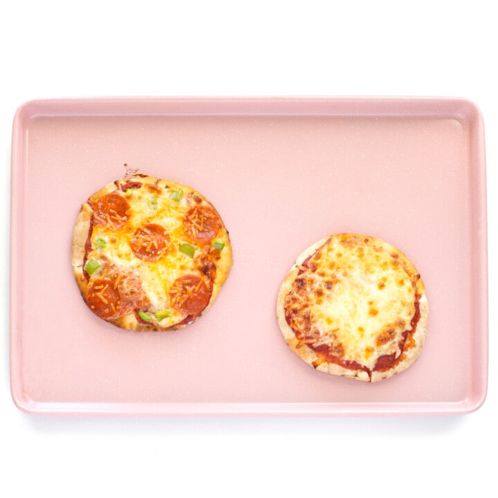 Baking pan with 2 cooked pita pizzas with varies toppings.