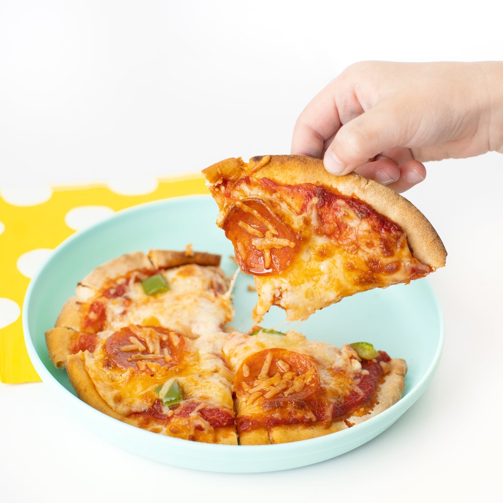 A hand holding a piece of pita pizza over a kids teal plate.