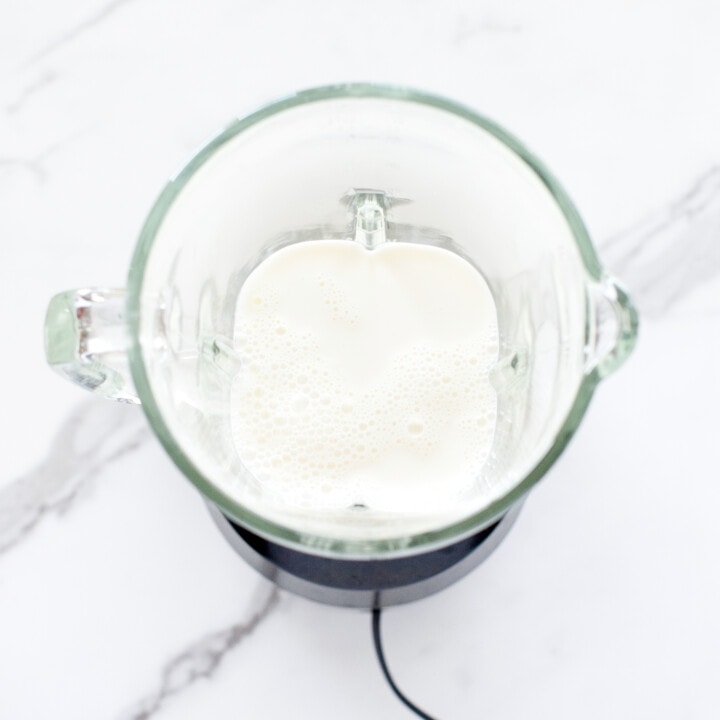 Clear blender on white marble counter with milk inside.