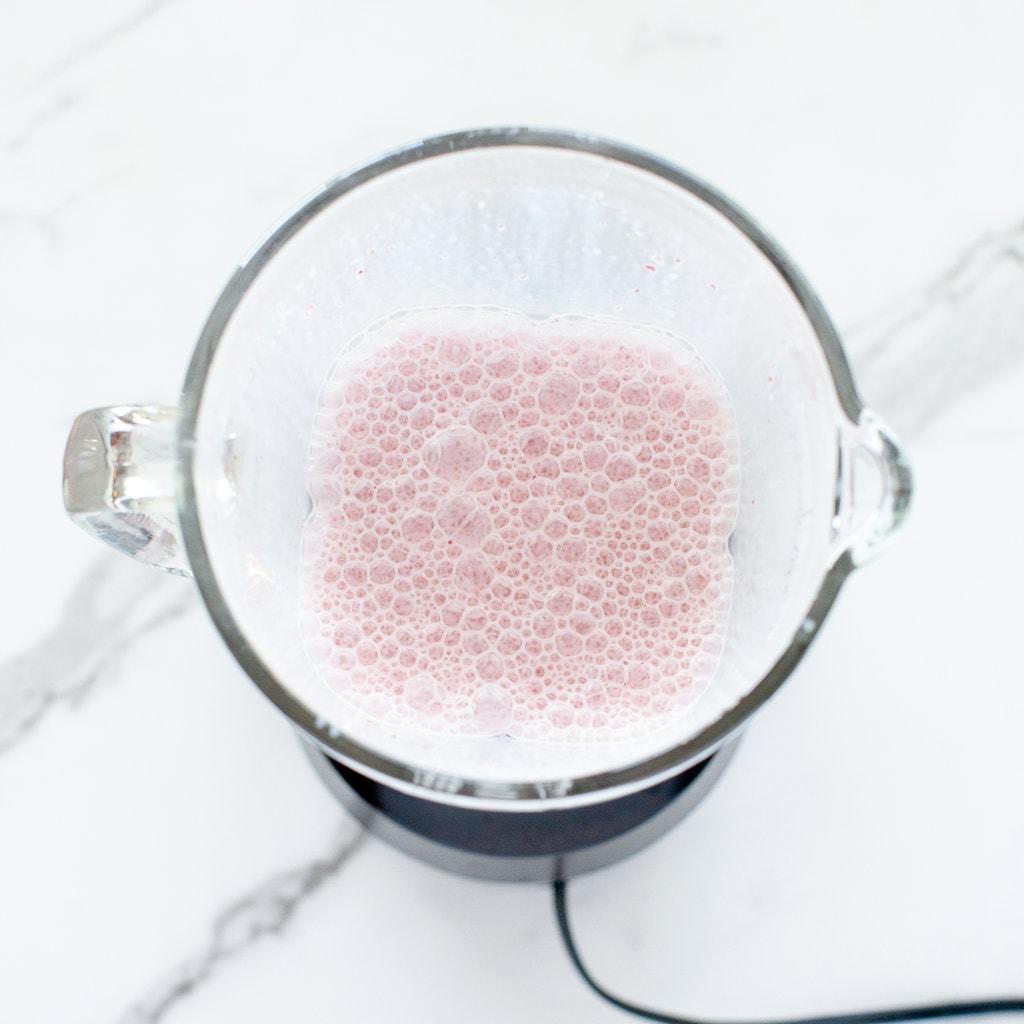 clear blender on a marble counter with strawberry milk inside.