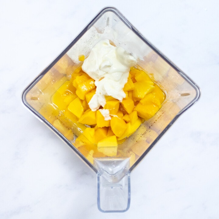 A clear blender with mango, yogurt, lime juice, and honey ready to be blended into Popsicles.