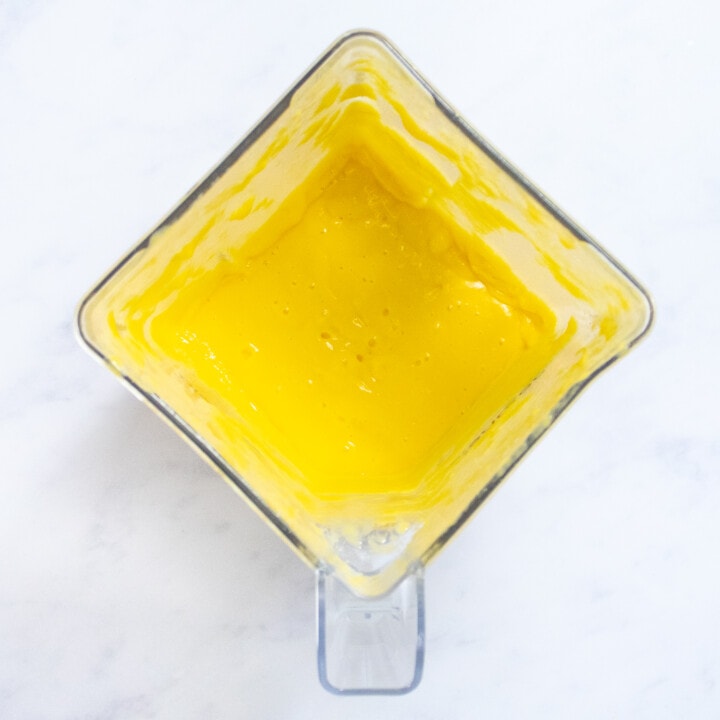 A clear blender with puréed mango ingredients getting ready to be poured into popsicle molds.