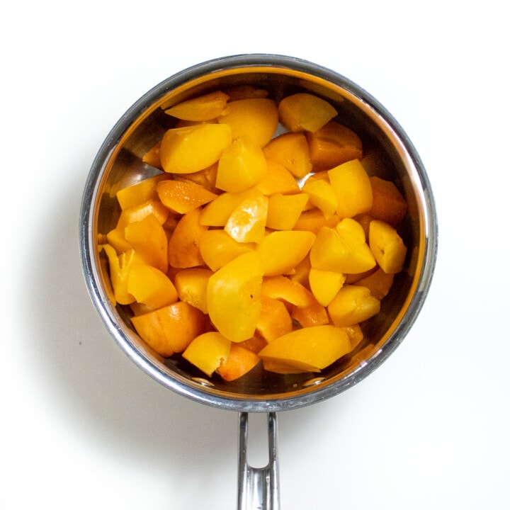 Hey small silver sauce pan filled with chopped apricots against a white background.