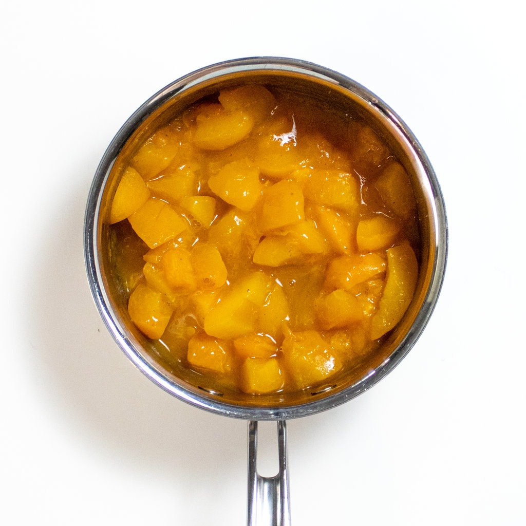 A small silver sauce pan full of summer apricots with cloves and water.