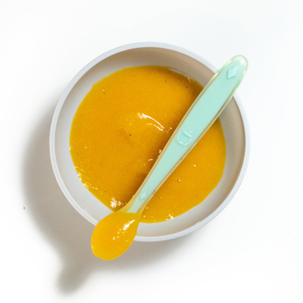 A gray baby bowl with a teal baby spoon with apricot. Against a white background.