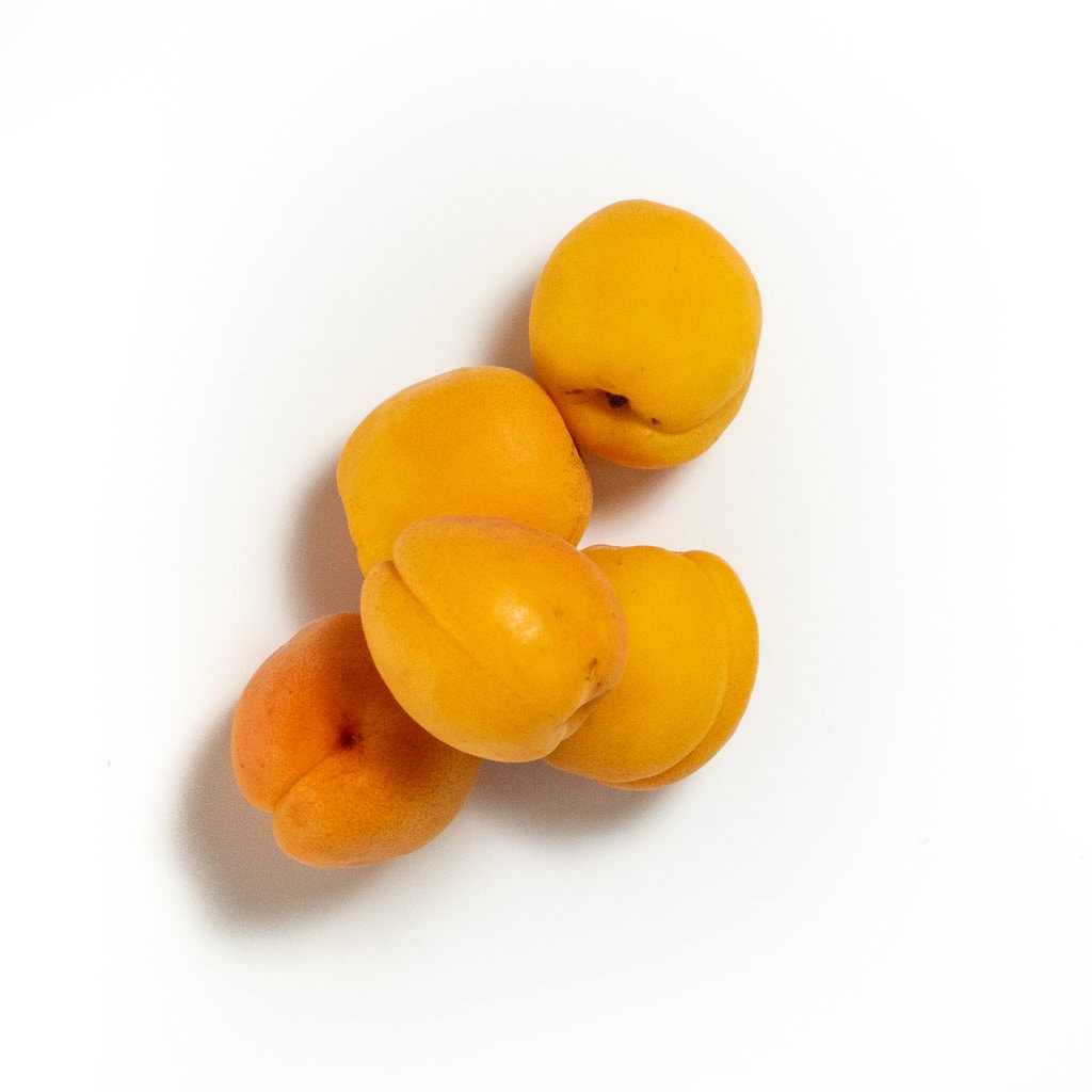 A pile of fresh apricots it's a white background.