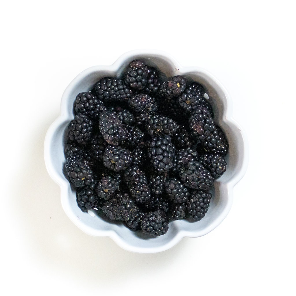 Blackberries in a bowl against a white backdrop.