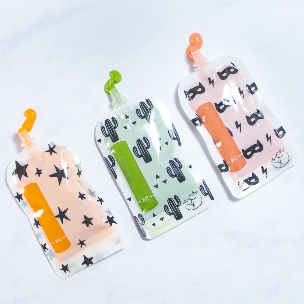 A row of baby food pouches with purée coming out of the tub against a white marble countertop.