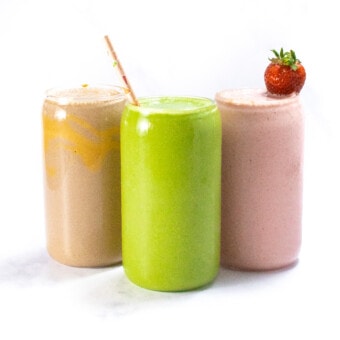 Three clear glasses full of smoothies for breast-feeding moms. One is green spinach and peach, one is pink which is a strawberry yogurt, and the other is chocolate peanut butter. All of his movies are against a white marble background.