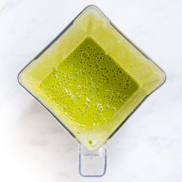 A clear blender on a marble countertop full of a green spinach smoothie for lactating moms.