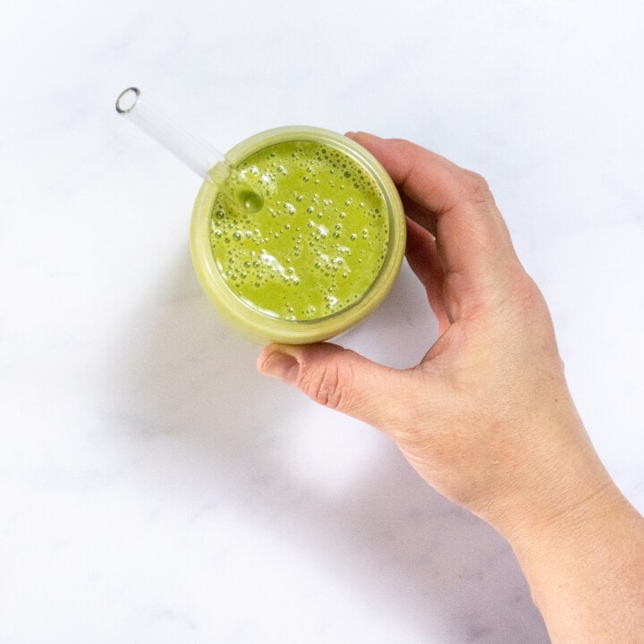 Hand reaching for a clear glass full of a green lactation smoothie for breast-feeding moms.