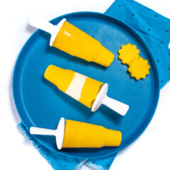 A dark blue plate full of three mango popsicles and a cut out with mangos.
