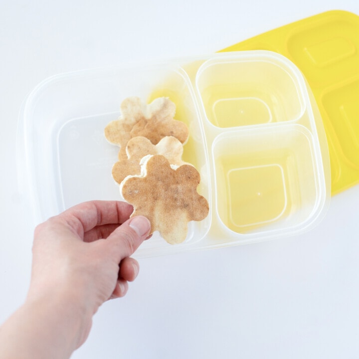 Hand packing cut out keto bread into a lunchbox for kids against a white background.