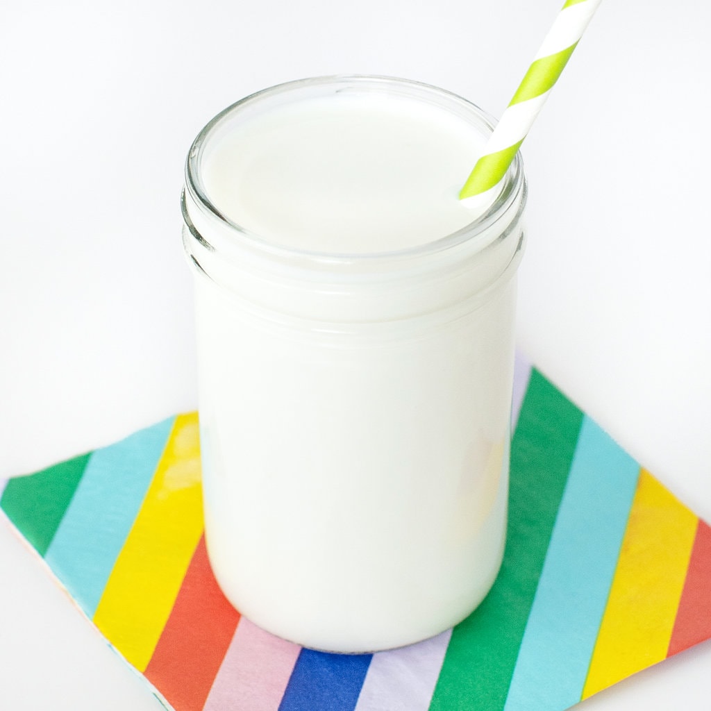 Clear glass full of vanilla milk with on top of a striped napkin with a striped straw.