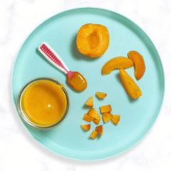 Blue baby plate on a white marble kitchen with apricots cut and pureed in different ways to serve to baby.