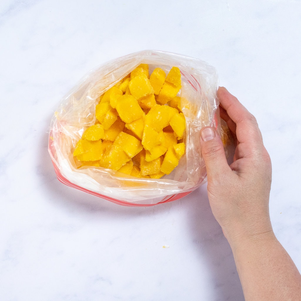 A hand holding a bag of frozen mango chunks.