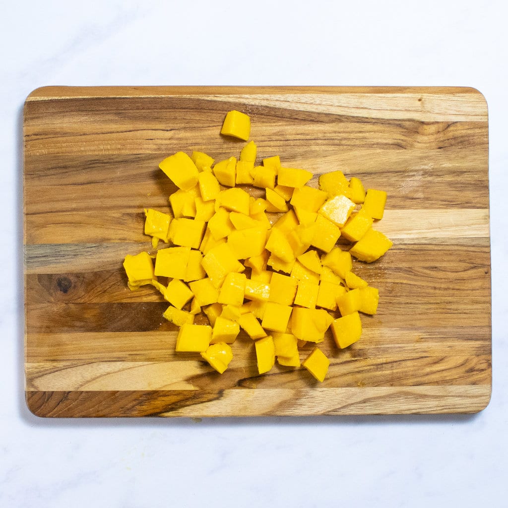 A wooden cutting board on a marble countertop with mango chunks.