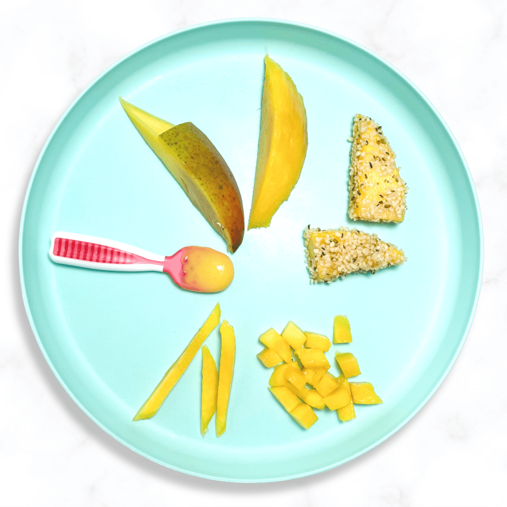 Teal baby plate with different ways to serve mango to your baby. The plate is sitting on a white marble counter in my kitchen.