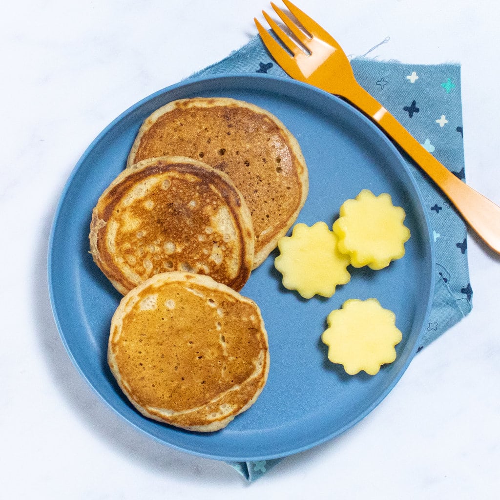 Three mango pancakes on a blue plate with mango cut outs in an orange fork.