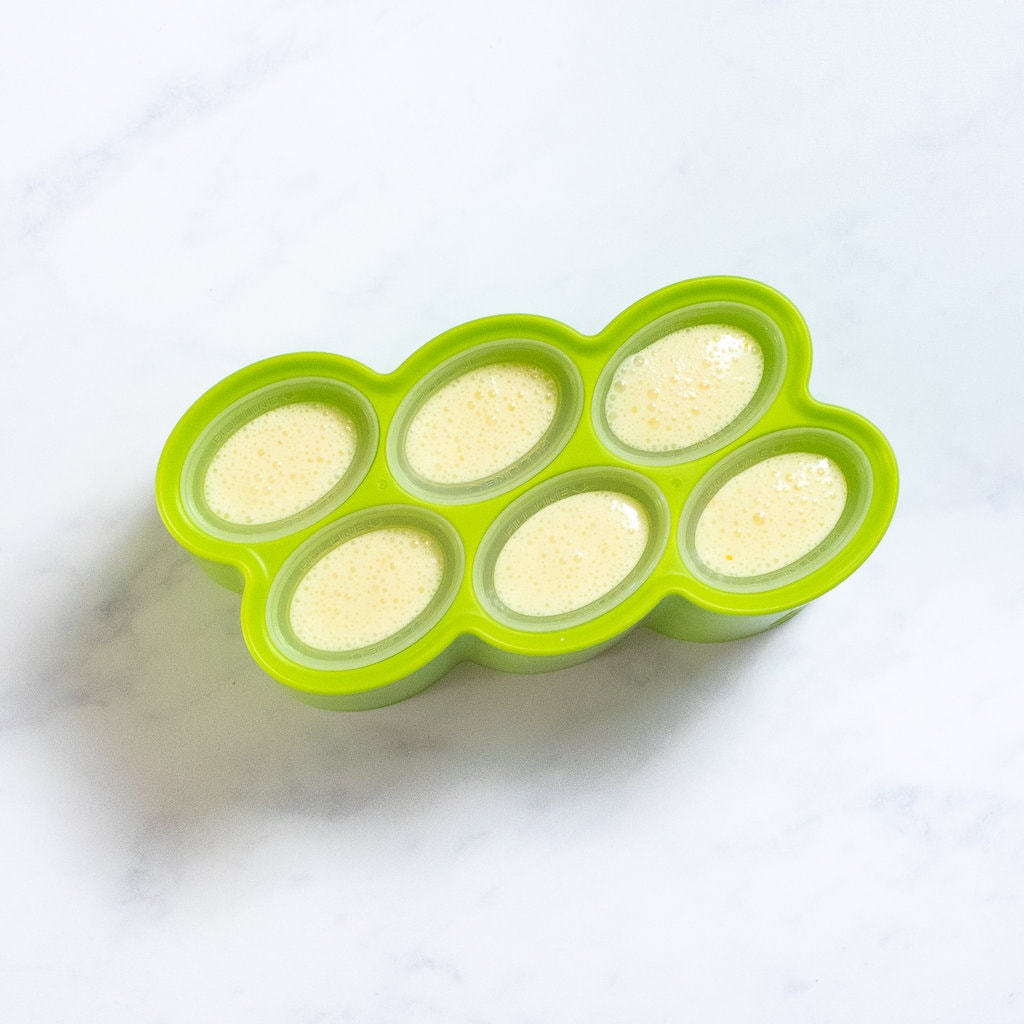 A green popsicle mold on a white marble counter full with orange Creamsicle mix.