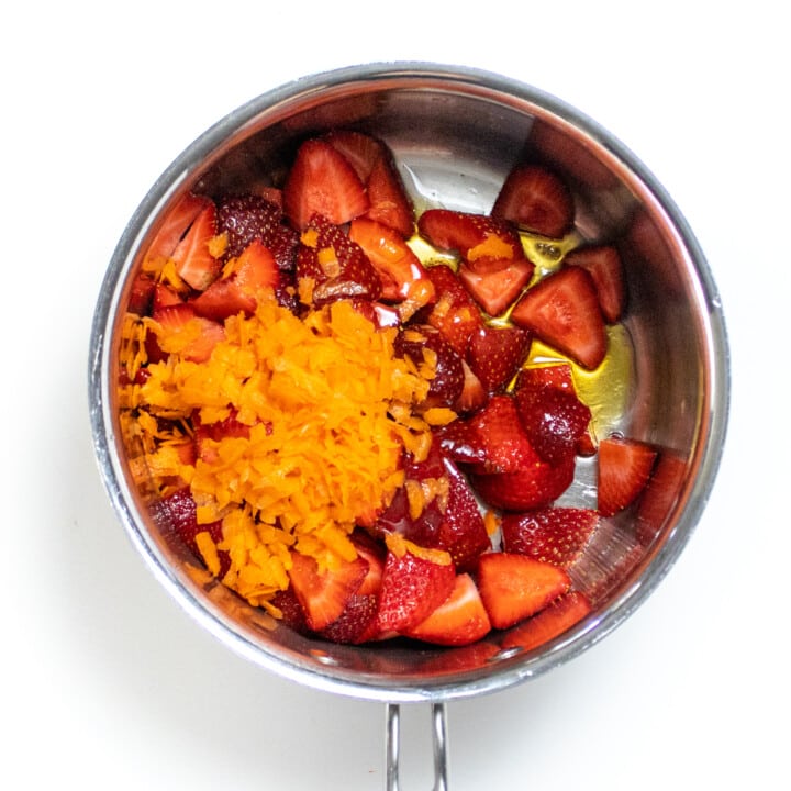 Silver sauce pan with strawberries, carrots and honey against a white background.