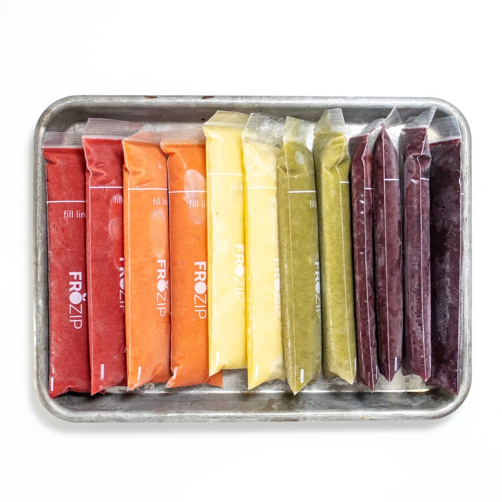 Selection of rainbow fruit freezer pops that are frozen on a baking sheet against a white background.