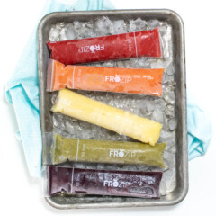 Small silver baking sheet with freezer pops in a rainbow color with ice and a blue napkin.