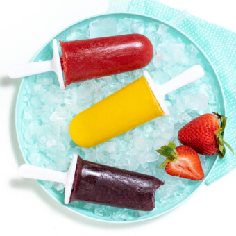 Blue plate with 3 different colors of popsicles over ice and a blue napkin.