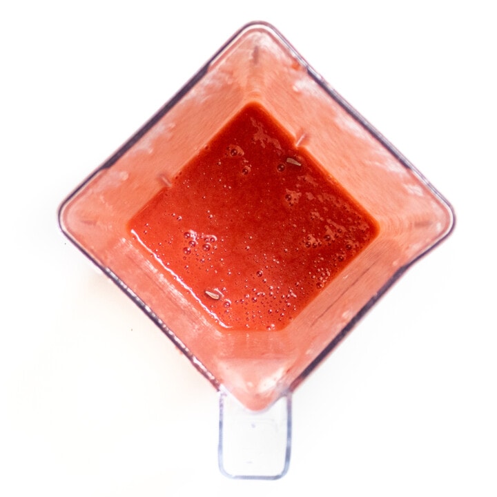 Clear blender full of a smooth strawberry puree that is ready to be poured into popsicle molds.