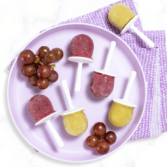 Kids purple plate sitting on a white marble counter with grape popsicles in two colors of popsicles on top. With a purple napkin under the plate.