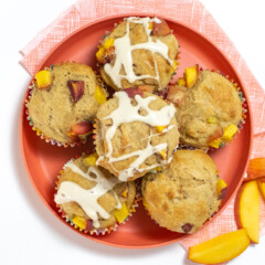 Pink kids plate with a pink napkin with peach muffins on top some of them with a cream cheese drizzle against a white background.