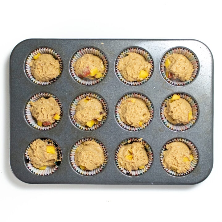A silver muffin tin filled with peach muffins ready to be baked.