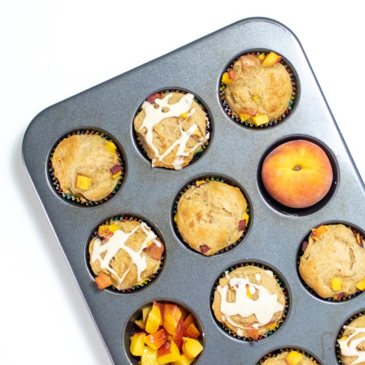 A muffin tin full of peach muffins some with a drizzle against a white background.