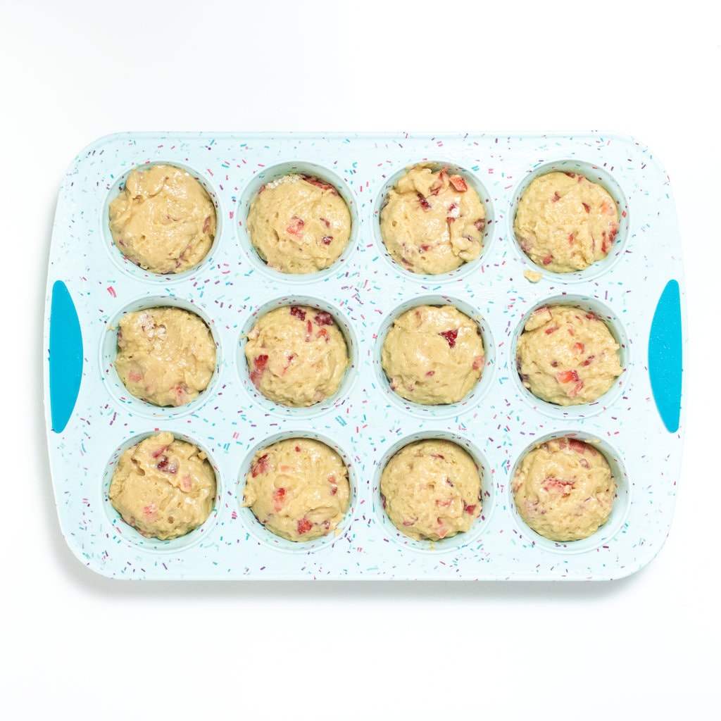 A blue muffin tin full with strawberry muffin batter against a white background.
