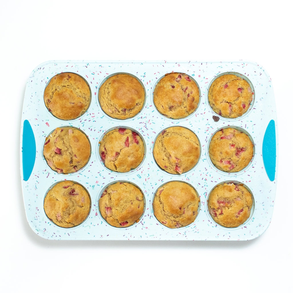 Cooked strawberry muffins in a blue muffin tin on a white background.