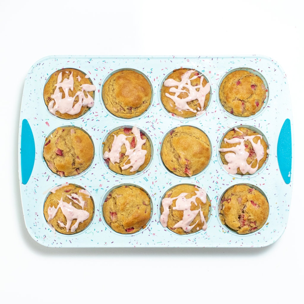A blue muffin tin on a white background with cooked a strawberry muffins with the cream cheese strawberry drizzle.
