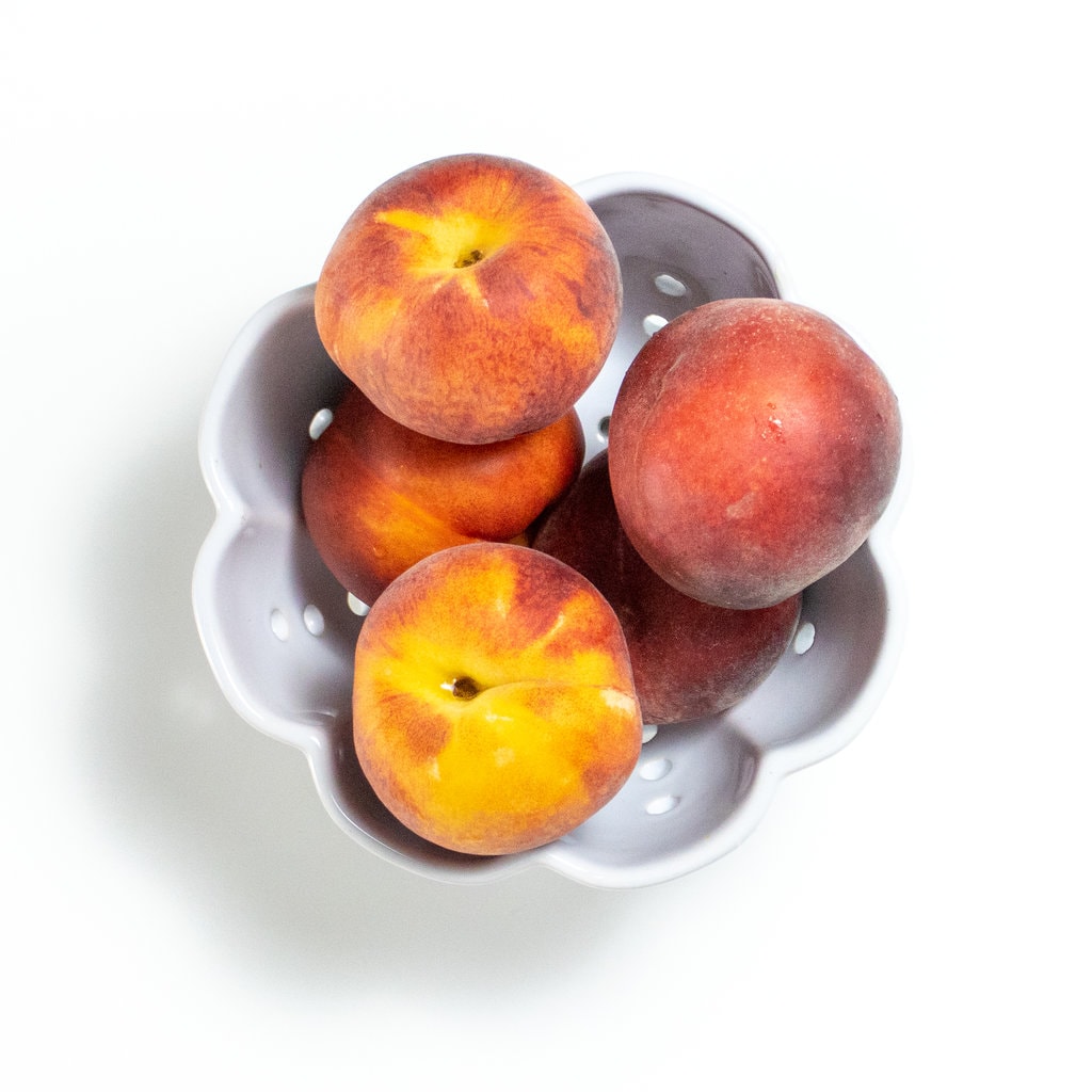 peaches in a bowl against a white background.