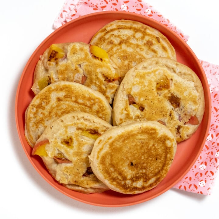 A pink kids play with a group of peach pancakes with a pink for compete against a white background.