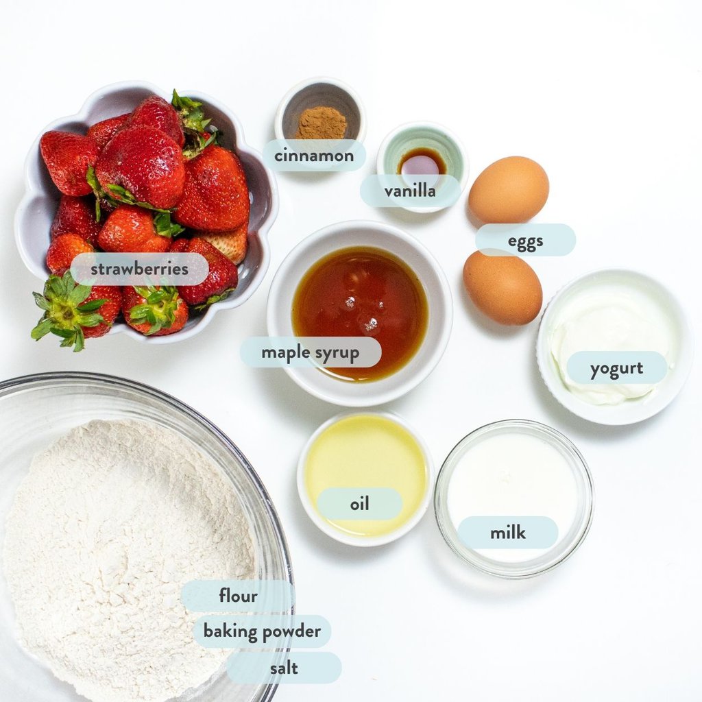 spread of ingredients for strawberry muffins on a white countertop with labels saying what each food item is.