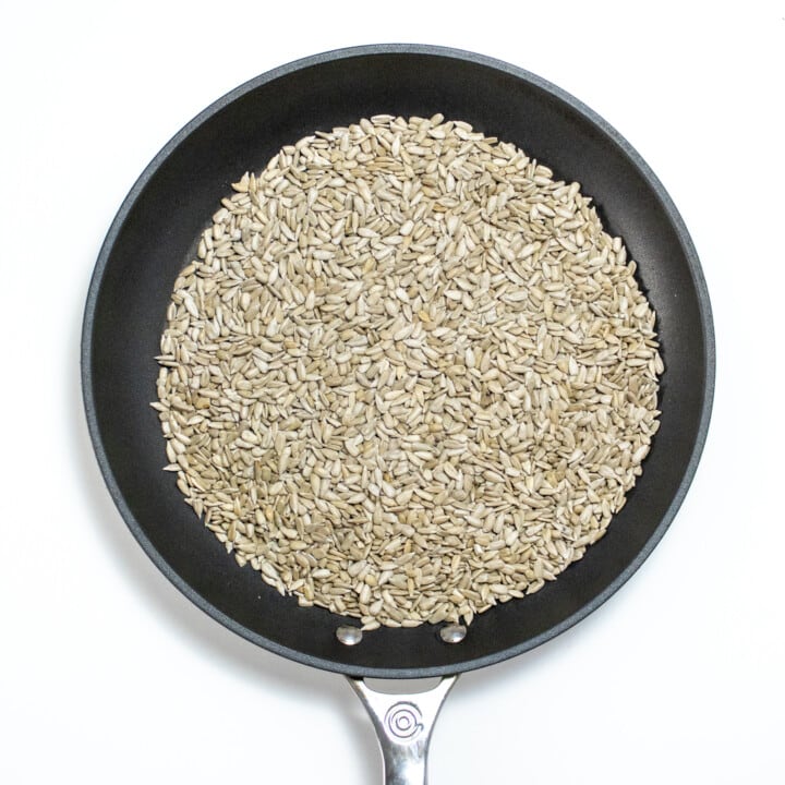 Is skillet against a white counter, filled with raw sunflower seeds.