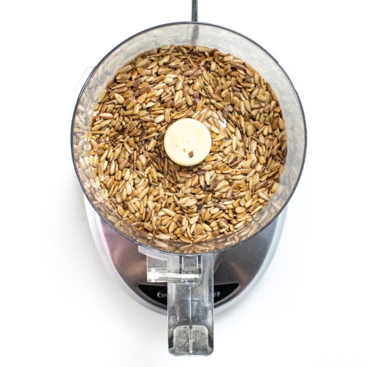 A food processor, full of toasted sunflower seeds against the white countertop.