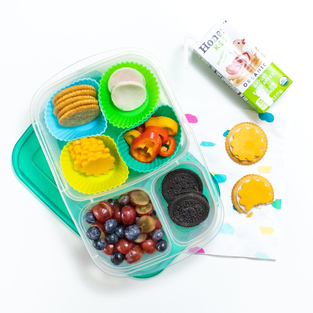 A spread of a kids lunch box and opened with homemade turkey and cheese lunchables with a napkin, juice and lunchables made and half eaten on a white counter.