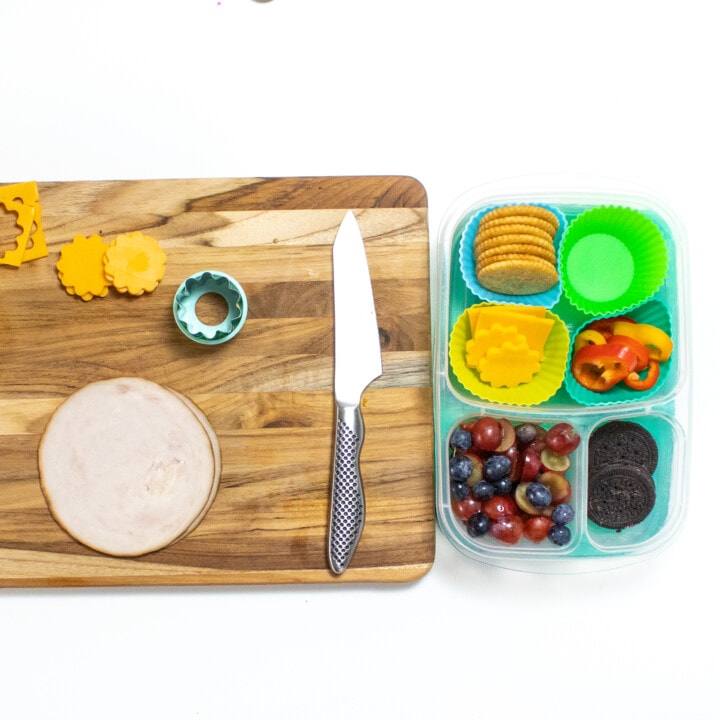 A wooden cutting board and a kids lunchbox being prepped for turkey lunchables.