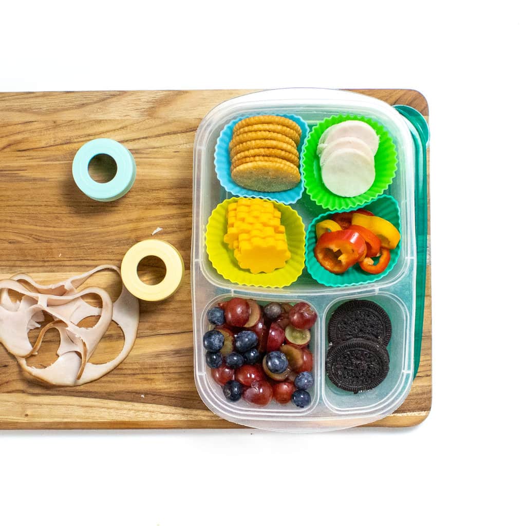 Wooden cutting board on a white countertop with a homemade kids lunchable on topp.