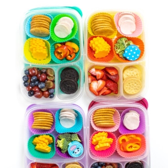 4 colorful kids lunch boxes lined up with turkey lunchables, fruit, veggies and sides.