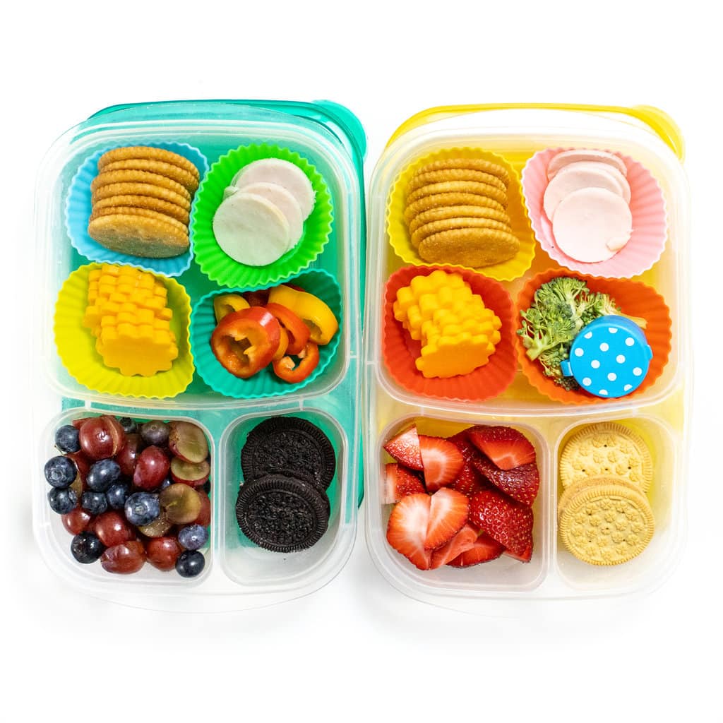 two different colorful kids lunch boxes lined up with turkey, cheese, crackers, fruit, veggies and cookies.